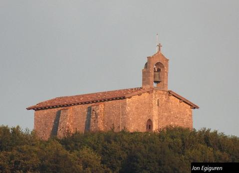 Ilunabarreko eguzkiaren azken izpien kolore bereziekin  ikusten da ermita Aizarnatik. Edozein aldetik begiratuta ere beti polita ikusten da ermita zahar hau.  Aizarnatik aterata dago argazkia 